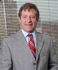 imagen frontal de frank baer en la que aparece sonriente con traje y corbata